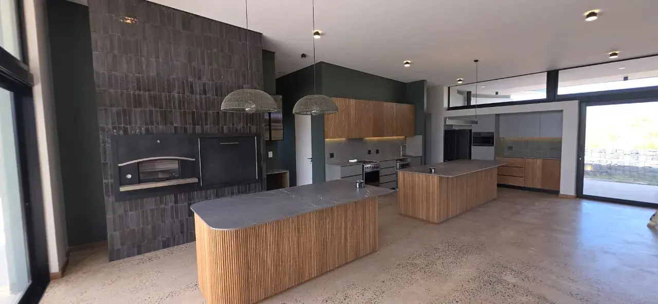 JehCon kitchen renovation with two fluted oak islands, dark stone worktops, a tiled indoor braai wall and a polished concrete floor