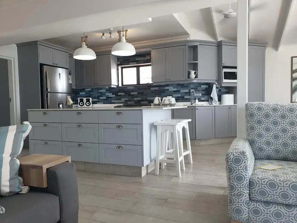 JehCon grey Shaker-style kitchen renovation with a blue subway tile splashback, pendant lights and a large drawer island