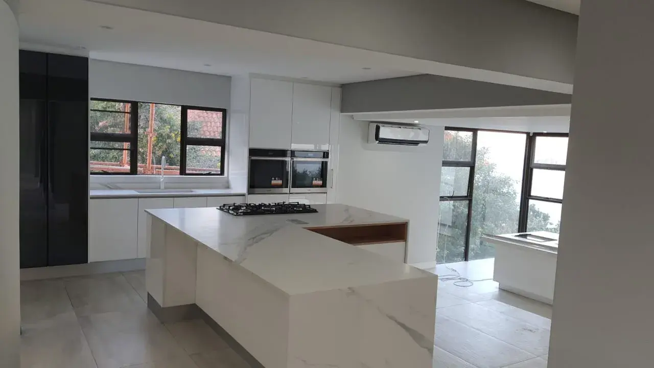 JehCon kitchen renovation with a marble-look waterfall island, built-in gas hob, eye-level double ovens and white gloss handle-less cabinetry