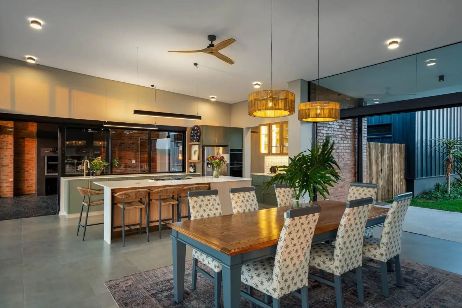 JehCon kitchen renovation with sage green cabinetry, an oak island with a white quartz top, rattan pendant lights and an open-plan dining area