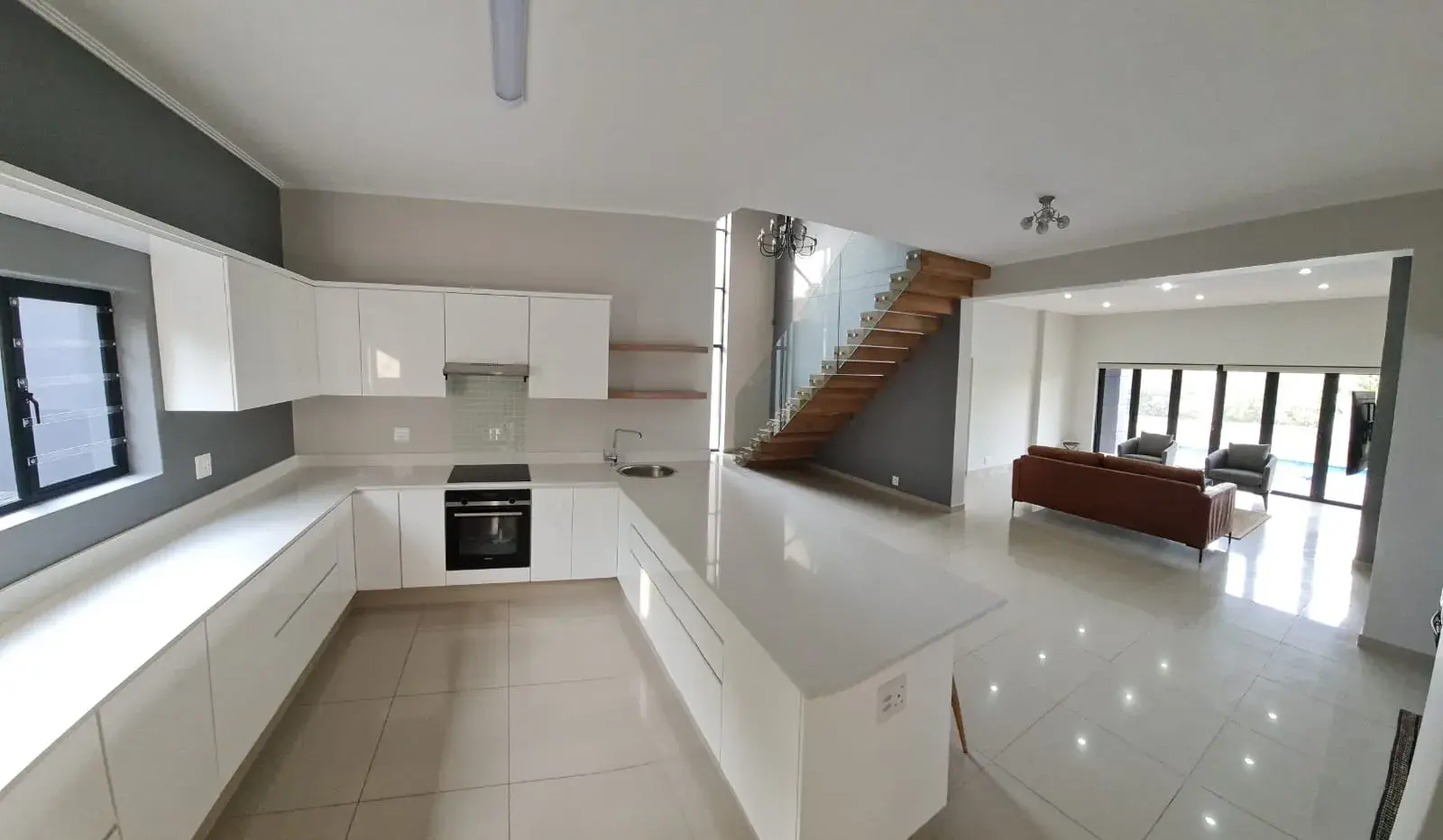 JehCon white gloss U-shaped kitchen renovation with quartz worktops, a built-in oven and a breakfast counter opening onto the living area